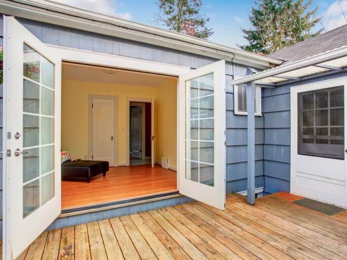 This is an image of a deck next to a blue house with it's white doors open.