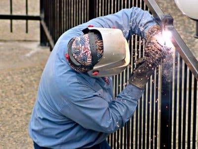 This image shows a fence contractor welding a new iron fence on a commercial property in North Carolina.