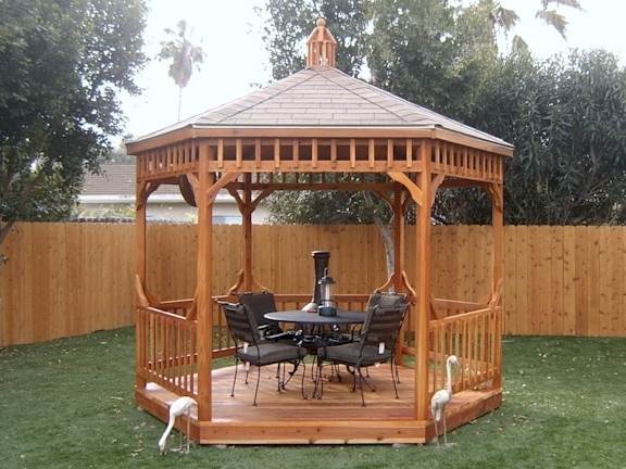 This image shows a gazebo with a table and chairs inside in a residential back yard.